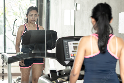 Young woman practicing in the gym with mirrors. Girl walking on treadmill at fitness club.