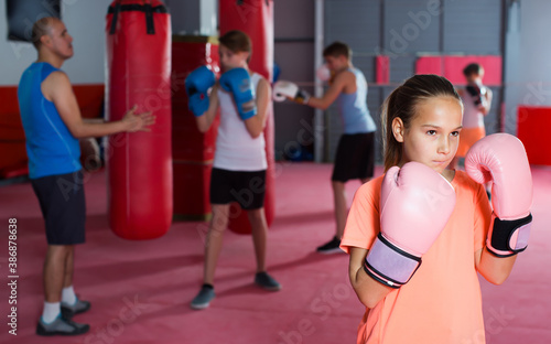 Portrait of cheerful girl boxer wearing rose gloves in boxing hall