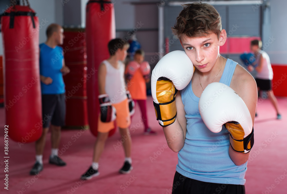 Boy boxer in gloves posing during boxing exercising at gym