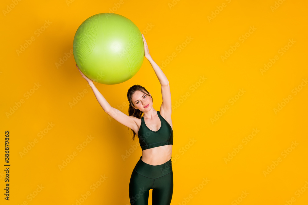 Portrait of attractive sportive girl holding in hands fitball over head doing incline mat work slimming figure isolated bright yellow color background Portrait of attractive sportive girl holding in hands fitball over head doing incline mat work slimming figure isolated bright yellow color background