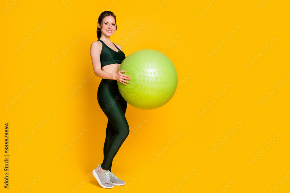 Full length body size view of nice slender cheerful girl holding in hands fitness ball isolated over bright yellow color background Full length body size view of nice slender cheerful girl holding in hands fitness ball isolated over bright yellow color background
