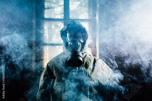 Φωτογραφία Spooky person with gas mask holding a lamp in dense fog in an abandoned building with eerie feeling