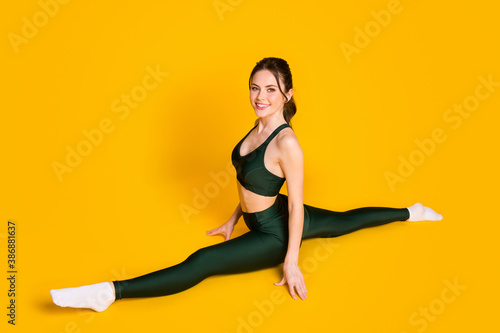 Lady trainer gym practice yoga sit floor stretch legs twine wear sports suit isolated yellow color background