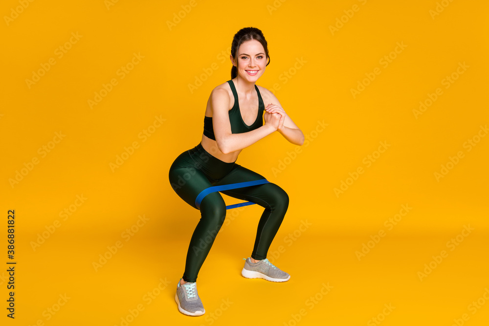 Full length photo of sporty lady stretch resistance rubber stripe doing squats sports suit isolated yellow color background