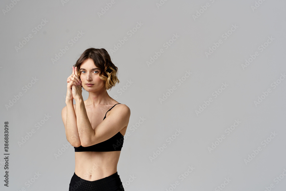 Naklejka premium A slender woman in black leggings on a gray background gestures with her hands gymnastics sports