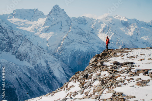 Winter traveler in the mountains. Tourist on the cliff. Mountains in the snow background.
