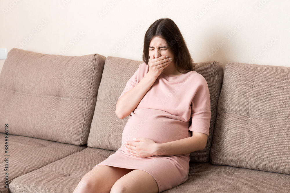 Young vomiting woman sitting on sofa and suffering with nausea. Pregnancy expectation concept, copy space Young vomiting woman sitting on sofa and suffering with nausea. Pregnancy expectation concept, copy space
