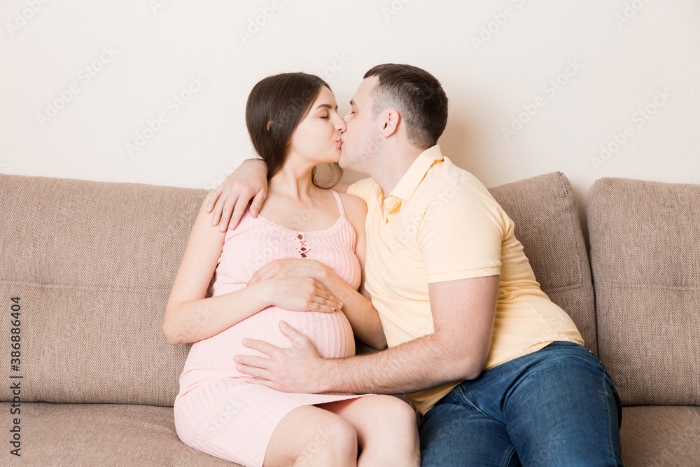 Young family. Attractive pregnant woman and man resting on bed and kissing. Happy pregnant family Young family. Attractive pregnant woman and man resting on bed and kissing. Happy pregnant family