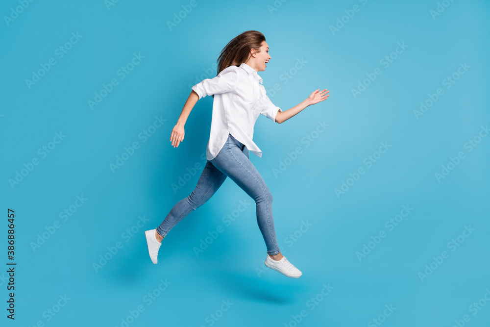 Full length profile photo of lady jumping high up running wear white shirt jeans shoes isolated blue color background