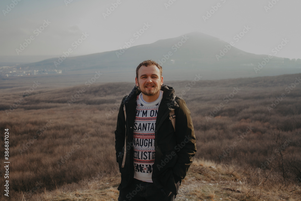 A man in a Christmas sweater against a background of mountains.