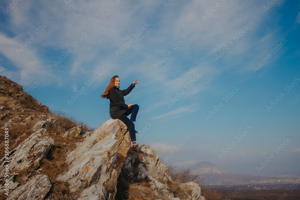 Fototapeta premium A young woman sits high on a mountain against a blue sky.
