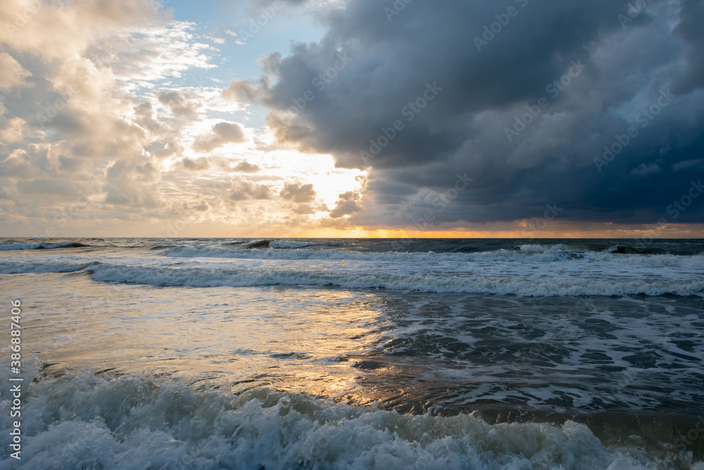 Sunset on the North Sea near the town of Petten, with dark colored clouds and an orange setting sun