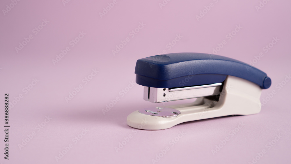 Blue stapler isolated on a purple background. Office supplies. Stapler, staple, paper, cardboard, office equipment Blue stapler isolated on a purple background. Office supplies. Stapler, staple, paper, cardboard, office equipment