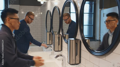 Diverse men washing hands in washroom sink of business center or restaurant