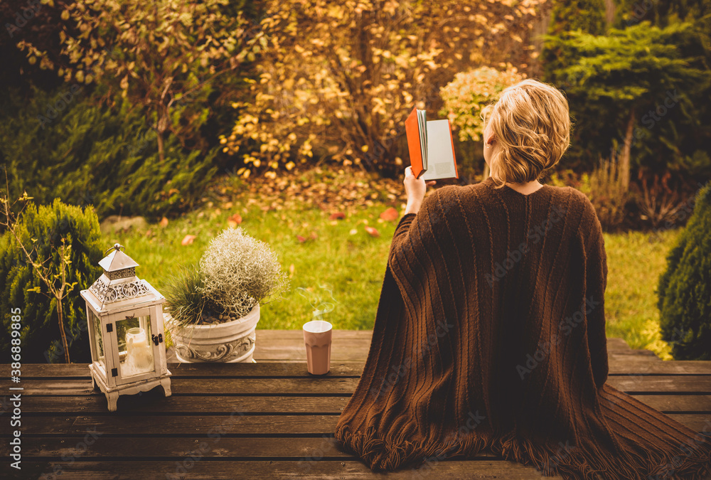 Woman reading book outdoor on the autumn garden terrace - leisure.