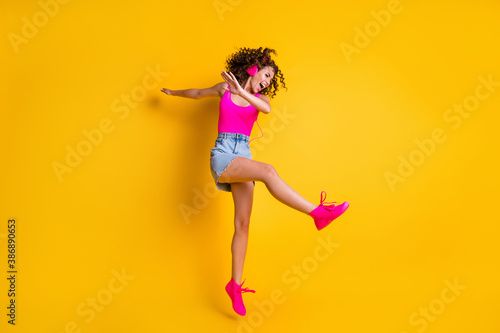 Fototapeta Naklejka Na Ścianę i Meble -  Full body profile photo of charming crazy lady jump high carefree listen earphones modern technology dancing dab wear pink tank top mini skirt shoes isolated bright yellow color background