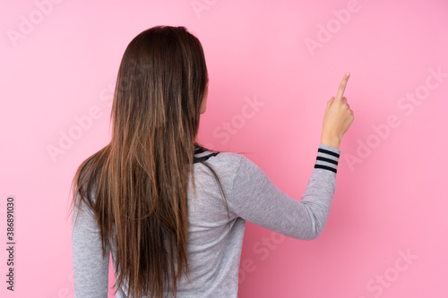 Teenager girl over isolated pink background pointing back with the index finger