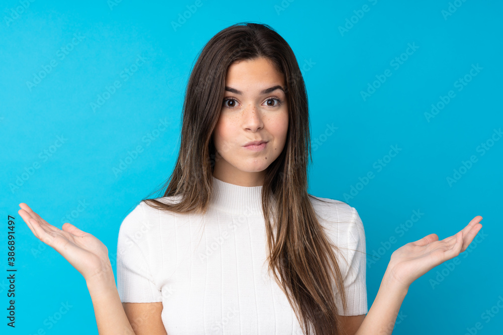 Fototapeta premium Teenager girl over isolated blue background having doubts while raising hands
