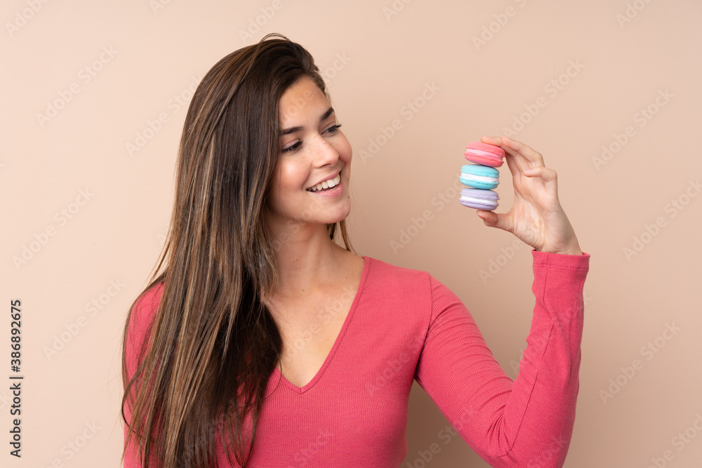 Teenager girl over isolated background holding colorful French macarons and with happy expression Teenager girl over isolated background holding colorful French macarons and with happy expression