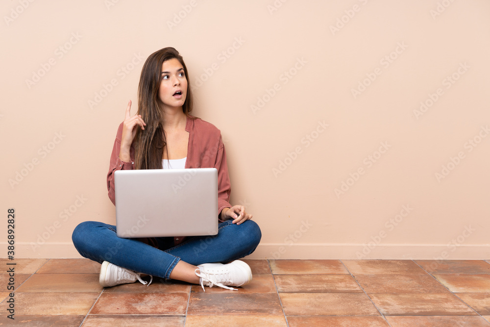 Teenager student girl sitting on the floor with a laptop thinking an idea pointing the finger up Teenager student girl sitting on the floor with a laptop thinking an idea pointing the finger up