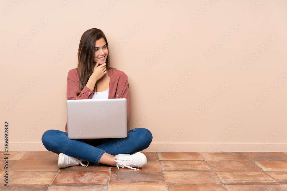 Teenager student girl sitting on the floor with a laptop looking to the side Teenager student girl sitting on the floor with a laptop looking to the side