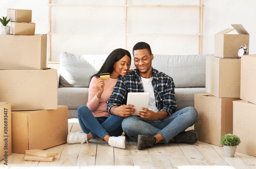 Young black couple using laptop computer and credit card for online shopping at their new home on moving day Young black couple using laptop computer and credit card for online shopping at their new home on moving day