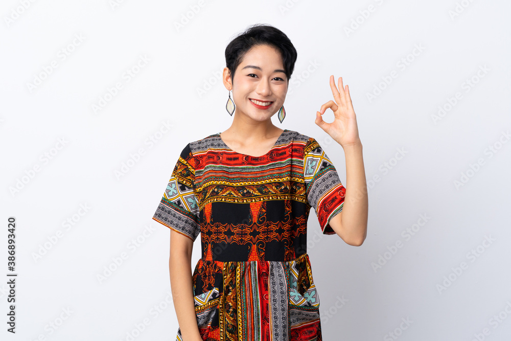 Young Asian girl with a colorful dress over isolated white background showing ok sign with fingers Young Asian girl with a colorful dress over isolated white background showing ok sign with fingers