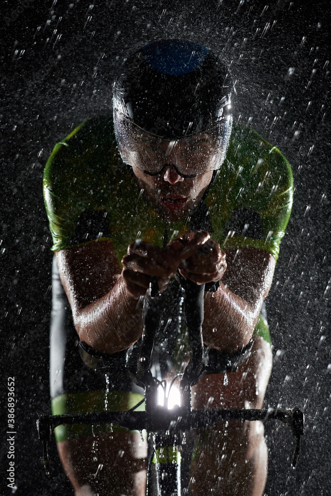 triathlon athlete riding bike fast on rainy night