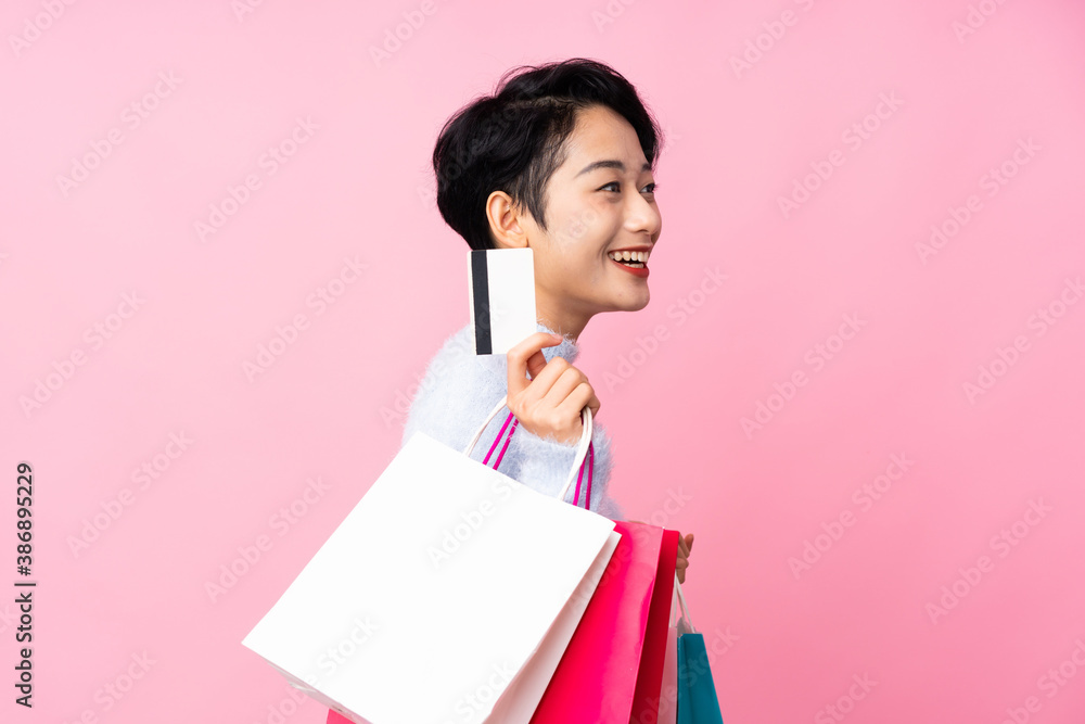 Young Asian girl over isolated pink background holding shopping bags and a credit card Young Asian girl over isolated pink background holding shopping bags and a credit card
