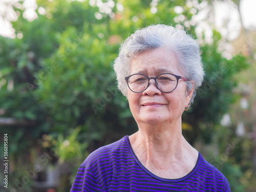 Portrait of a senior Asian woman wearing glasses, smiling and looking at camera while standing in a garden. Space for text. Concept of old people and healthcare