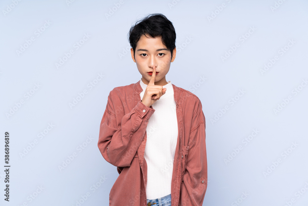 Young Asian girl over isolated blue background showing a sign of silence gesture putting finger in mouth Young Asian girl over isolated blue background showing a sign of silence gesture putting finger in mouth