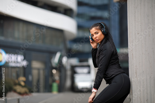 Young woman in black sportswear ready for jogging in the city listens to music through headphones