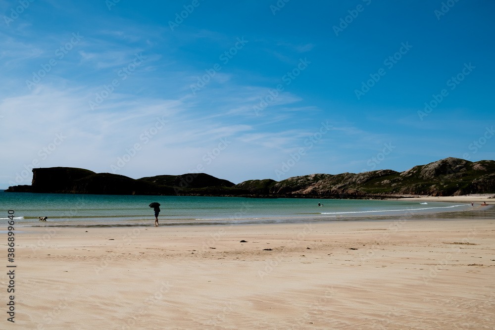 Oldshoremore beach, Scotland with silhouette of man with umbrella and dog