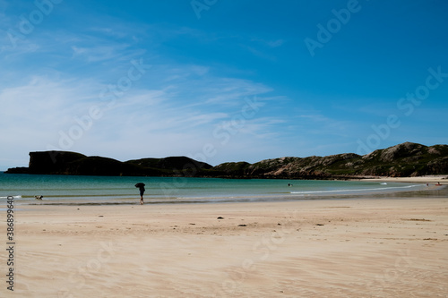 Oldshoremore beach  Scotland with silhouette of man with umbrella and dog