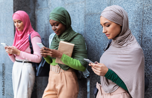 Modern Arab Ladies Using Smartphones Standing Over Gray Wall