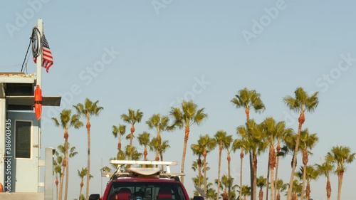 Iconic retro wooden lifeguard watch tower, baywatch red car. Life buoy, american state flag and palm trees against blue sky. Summertime california aesthetic, Santa Monica beach, Los Angeles, CA USA.