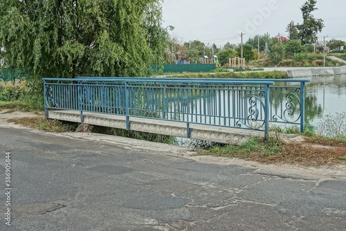 concrete pedestrian bridge with blue metal handrails by a gray asphalt road on the shore of a reservoir