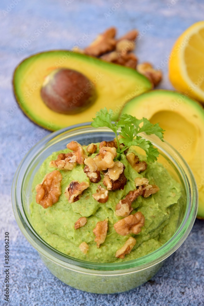 Avocado sauce with walnut and parsley in glass jar. Blue background