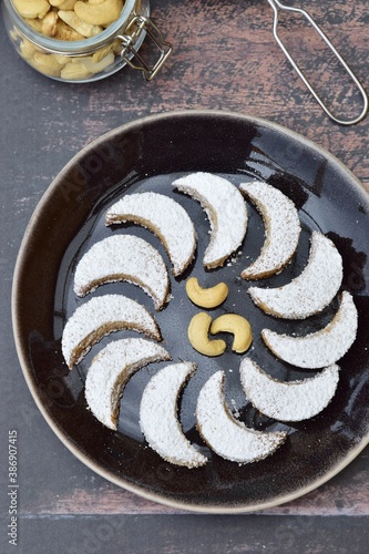 Putri Salju Kacang Mede or crescent-shaped cookies with cashew coated with powdered sugar. Popular Indonesian dessert to celebrate Eid al Fitr or Idul Fitri. Dark brown background