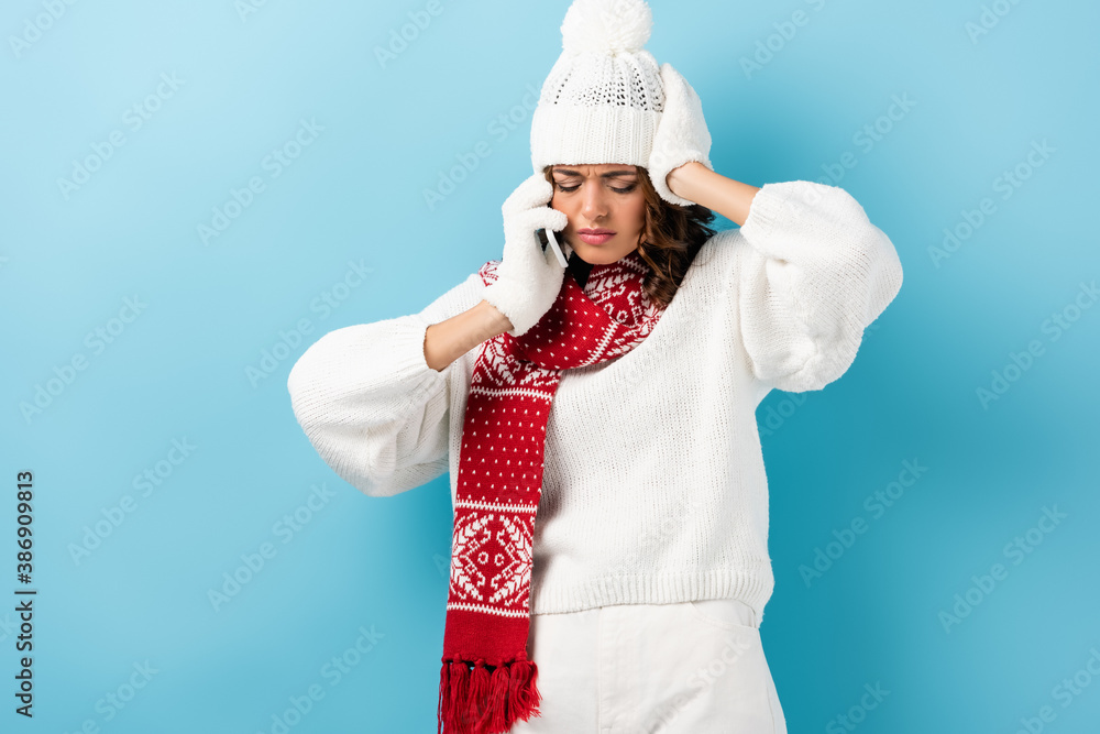 upset young woman in white winter outfit talking on smartphone on blue upset young woman in white winter outfit talking on smartphone on blue