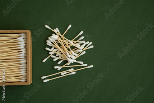 Eco-friendly cotton swabs. A cardboard box containing recyclable bamboo cotton buds on a green surface. Zero waste concept. Eco product. Cosmetic sticks in a box. Wooden sticks for cleaning ears.