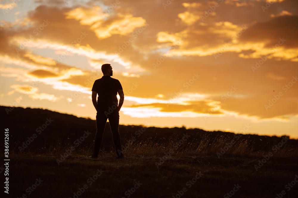 Back view of the silhouette of a man standing on a mountain at sunset. A view of the magical sky at sunset in nature