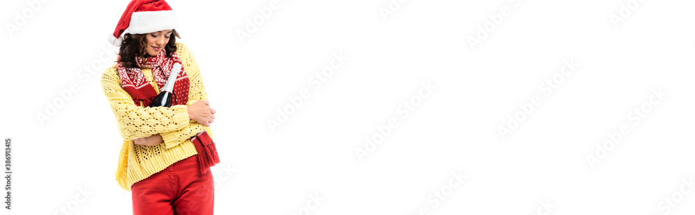 panoramic concept of young woman in santa hat and scarf with ornament holding bottle of champagne isolated on white panoramic concept of young woman in santa hat and scarf with ornament holding bottle of champagne isolated on white
