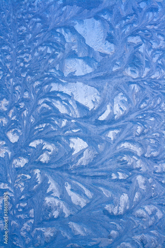 Ice pattern on glass. A beautiful drawing on a frozen window. Vertical.