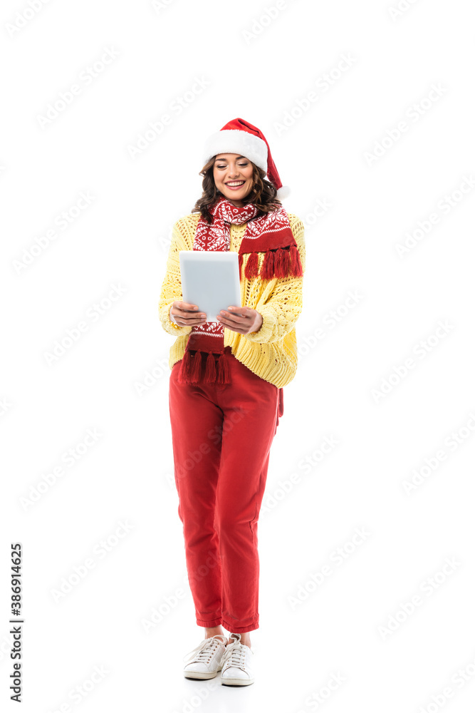 joyful young woman in santa hat and scarf looking at digital tablet isolated on white joyful young woman in santa hat and scarf looking at digital tablet isolated on white