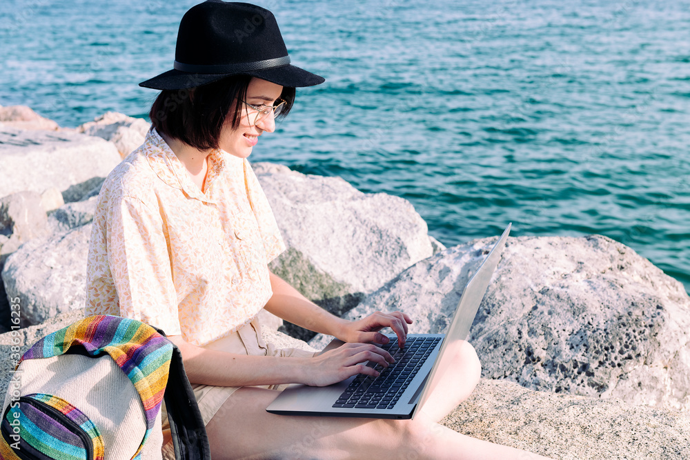 young woman with computer and backpack by the sea