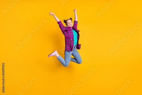 Full length photo of attractive crazy teen lady jump high up air flight ecstatic champion marathon sports competition wear casual plaid shirt shoes jeans isolated yellow color background