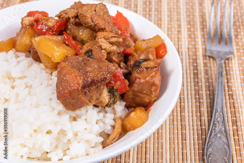 Adobo pork with pineapple and pepper in a bowl of boiled rice on a bamboo napkin, closeup - Philippine cuisine