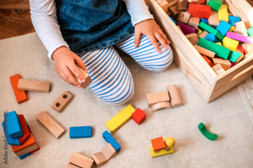 Little girl playing with wooden bricks at home.