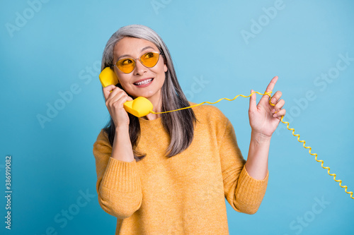 Photo of pretty charming aged woman calling friend ask new supermarket opened their street direct finger up playing wire wear sunglass yellow jumper vivid blue color background photo